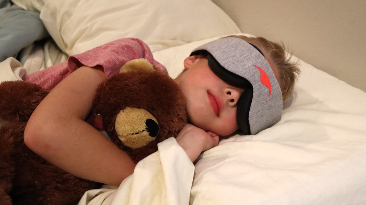 A boy sleeping with the Manta Sleep Mask and a teddy bear